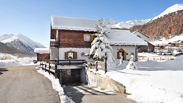 A wooden chalet with a snow-covered roof, a wooden fence, and a mountain backdrop. - Pet-friendly Holiday Home Baita sulle Alpi with Mountain View, Garden, Terrace, BBQ & Wi-Fi (livigno)