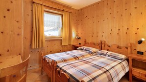 A wooden room with two beds, a window with curtains, a desk, and a nightstand. - Pet-friendly Holiday Home Baita sulle Alpi with Mountain View, Garden, Terrace, BBQ & Wi-Fi (livigno)