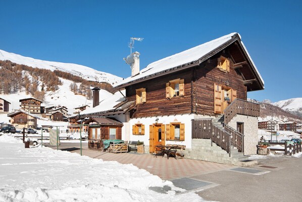 Eine Holzhütte mit einer Treppe zum Eingang, verschneitem Gelände und einem Berg im Hintergrund.