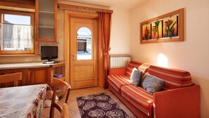 A cozy living room with a wooden door, a sofa, a table with a floral tablecloth, and a painting on the wall. - Pet-friendly Holiday Home Baita sulle Alpi with Mountain View, Garden, Terrace, BBQ & Wi-Fi (livigno)