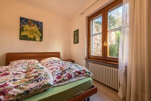 A bedroom with a bed, a window with curtains, a radiator, and two wall-mounted paintings.