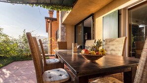 A patio with wicker furniture, a table with a fruit bowl, and a view of the garden.
