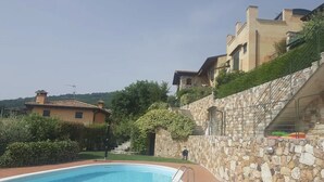 A pool area with a stone wall, a staircase, and buildings in the background.