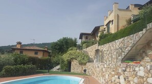 A pool area with a stone wall, a staircase, and buildings in the background.