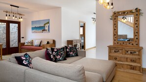 A living room with a sofa, wooden dresser, and a painting of a beach scene. - Villa Peaky with Sea & Mountain View, Pool & Sauna (Yazia)