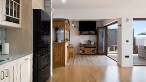 A modern kitchen with a black refrigerator, wooden cabinets, and a dining area with stools. - Villa Peaky with Sea & Mountain View, Pool & Sauna (Yazia)