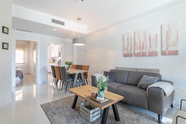 A modern living room with a sofa, a coffee table, and a dining area with chairs and a table.