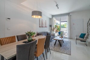 A modern living room with a dining area, a sofa, a coffee table, and a staircase.