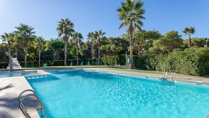 Une piscine d’un bleu éclatant, dotée d’un escalier en métal, entourée de palmiers et de verdure.