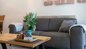 Un salon moderne avec un canapé gris, une table basse en bois agrémentée d  ’un objet décoratif et d’un vase de fleurs, ainsi que des œuvres d’art abstraites accrochées au mur.