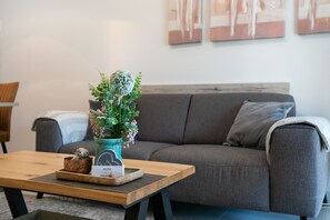 A modern living room with a grey sofa, a wooden coffee table with a decorative item and a vase of flowers, and abstract wall art.