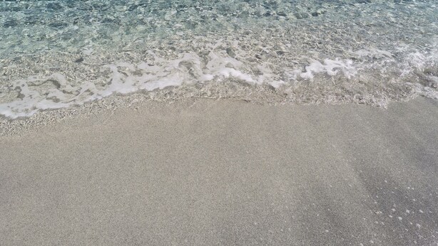 Una playa con agua cristalina, un promontorio rocoso y un barco a lo lejos.
