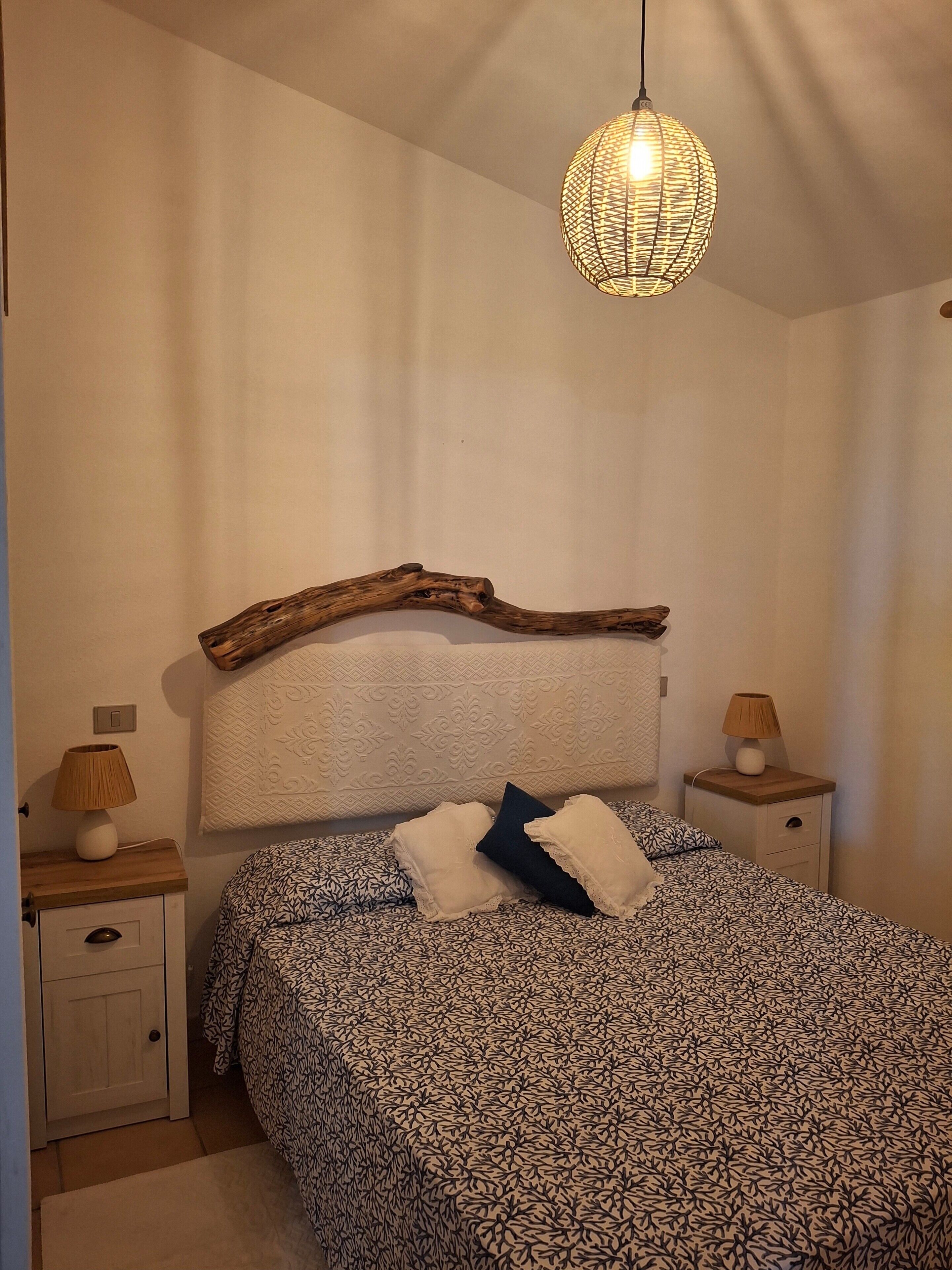 A bedroom with a bed, two bedside tables, a nightstand, a decorative branch headboard, and a hanging light fixture.