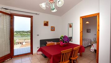 Uma sala de jantar com mesa posta para quatro pessoas, um sofá e uma varanda com vista.