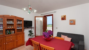 Un comedor con una mesa dispuesta para dos personas, un mueble de madera con puertas de cristal, un televisor y vistas al balcón.