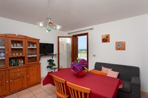 Un coin repas avec une table dressée pour deux personnes, un buffet en bois avec des portes en verre, un téléviseur et une vue sur le balcon.