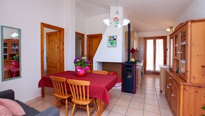 Comedor con una mesa lista para cuatro, sillas de madera, mantel rojo, candelabro y área de cocina con armarios y refrigerador.