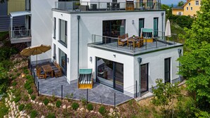 Una casa moderna de dos pisos con un balcón, mobiliario exterior y un patio cercado.
