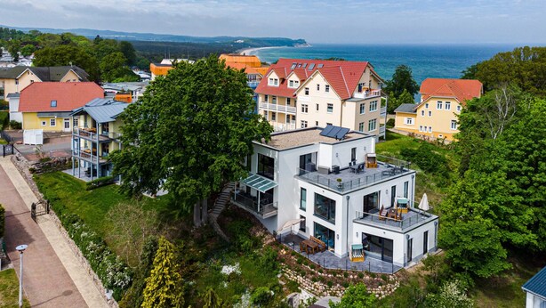 Una casa moderna con balc ón, rodeada de vegetación exuberante y vista al mar.