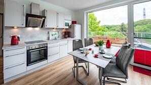 Una cocina moderna con armarios blancos, horno integrado y un comedor con mesa y sillas.