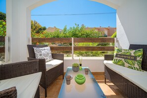 Eine Terrasse mit Korbmöbeln, einem Glastisch und Blick auf Grünflächen und Gebäude.