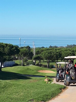 En golfbane med kig til havet, en golfbil og et velholdt grønt område.