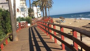Un paseo marítimo de madera que conduce a una playa con palmeras y un cielo azul despejado.