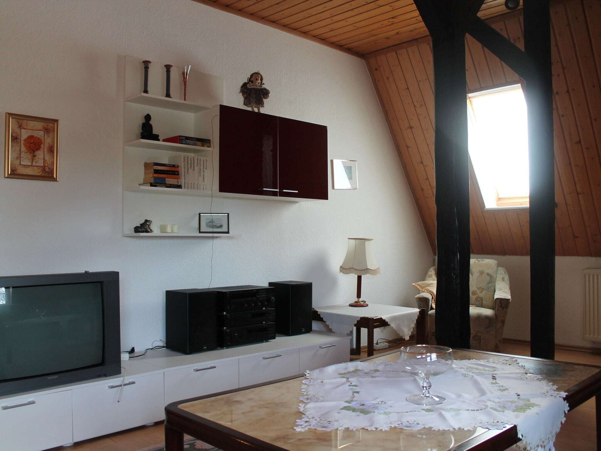 Un salon confortable avec un téléviseur, des meubles de rangement, une table avec un plateau en verre et une fenêtre laissant entrer la lumière naturelle.