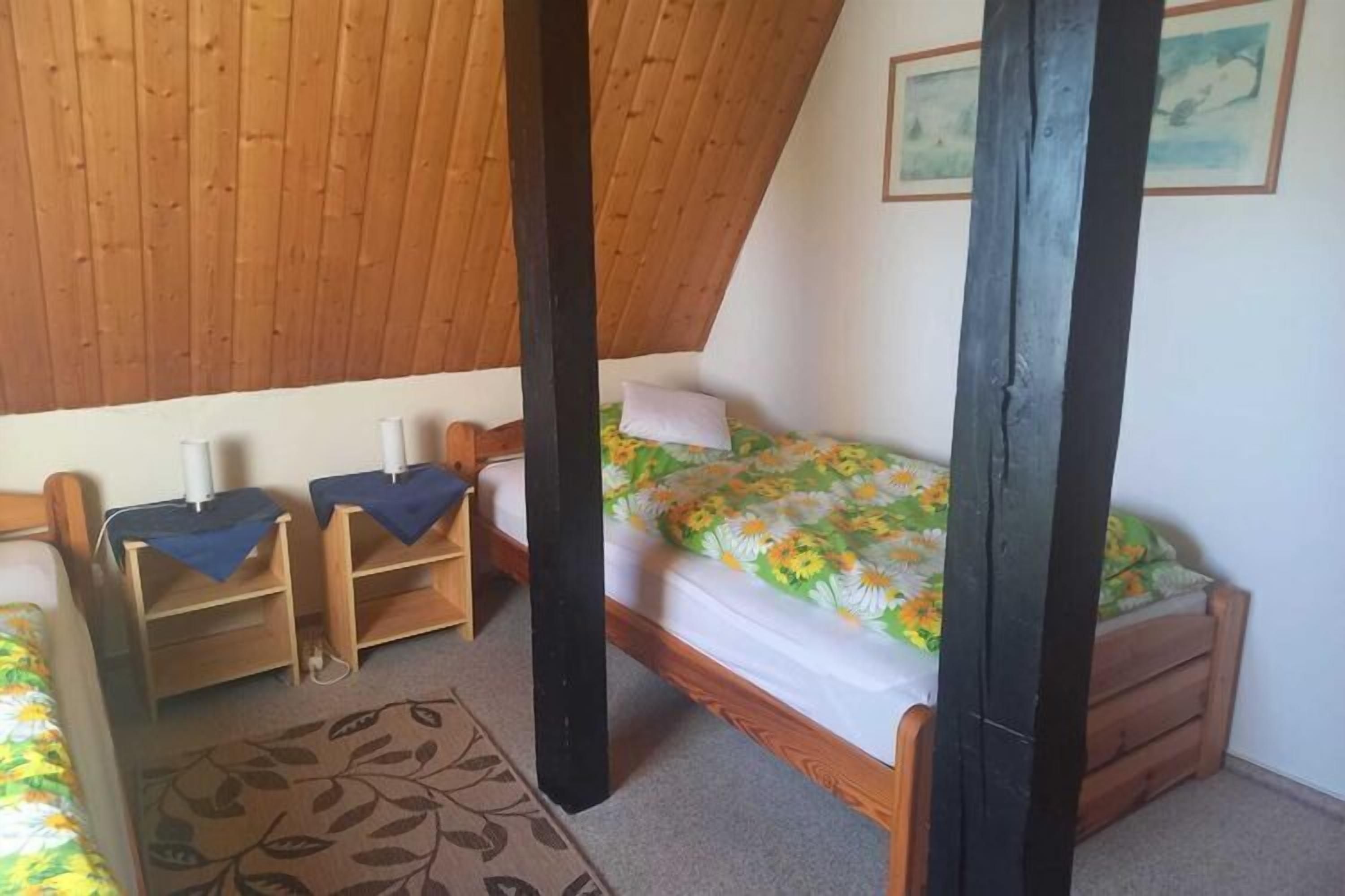 Une chambre avec un plafond en pente, un lit recouvert d’une couvre-lit à motifs floraux, deux tables de chevet avec des lampes et une tête de lit en bois.