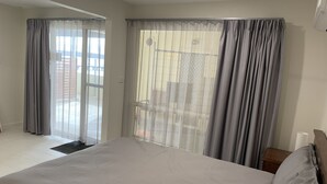 Un dormitorio con una cama grande, cortinas grises y vista a un edificio.
