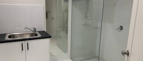 A modern bathroom with a glass-enclosed shower, a sink with a black countertop, and white cabinetry.