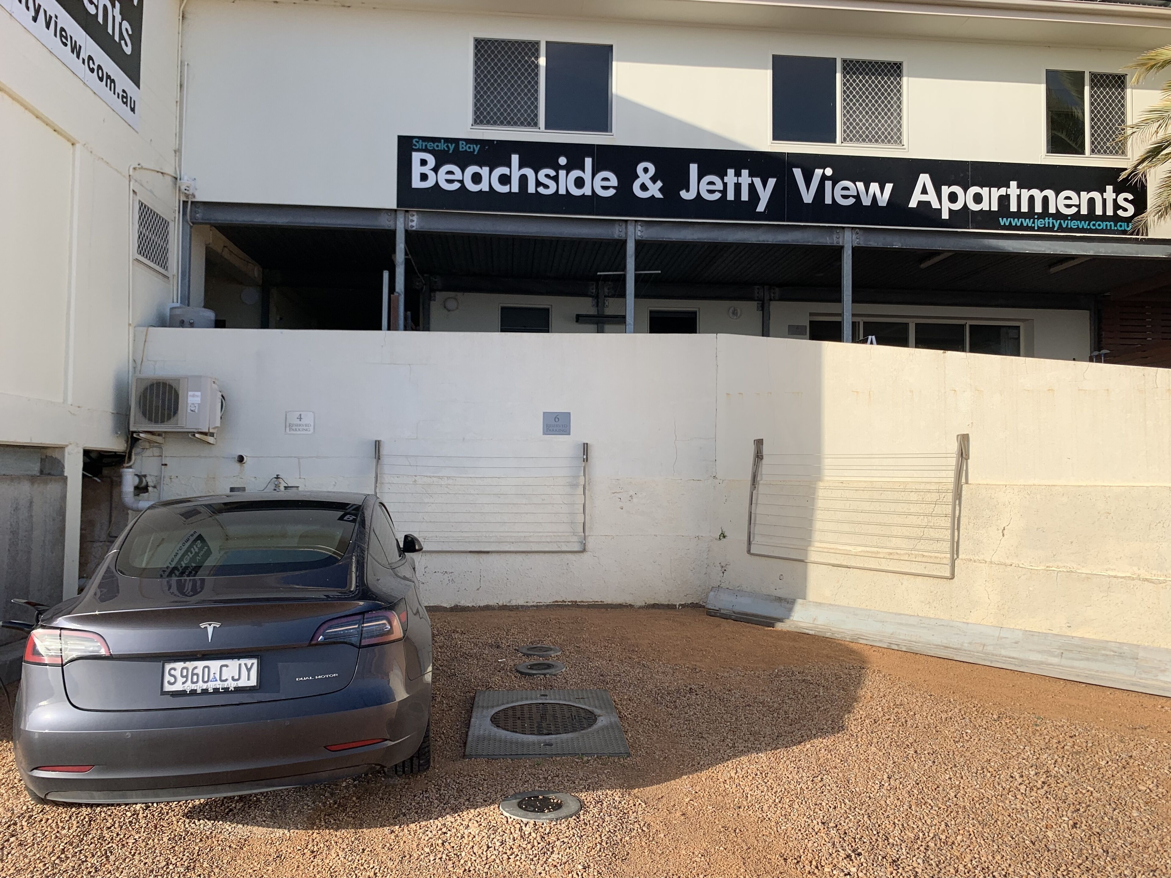 Een grijze Tesla staat geparkeerd voor Beachside & Jetty View Apartments.