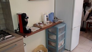 Cuina amb forlla de gas, cafetera, nevera, moble d'emmagatzematge blau i un ventilador.