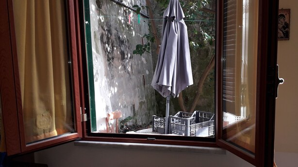 Habitació amb una finestra gran, una cadira i un escorredor amb roba.