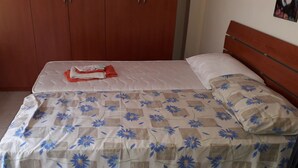 Un llit amb un estenat floral i una tovallola vermella ben arrugada a sobre.