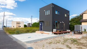 A modern two-story building with a flat roof, large windows, and a small outdoor seating area with a table and benches. - SEASIDE HOUSE YASUTAKETEI (Shirahama)