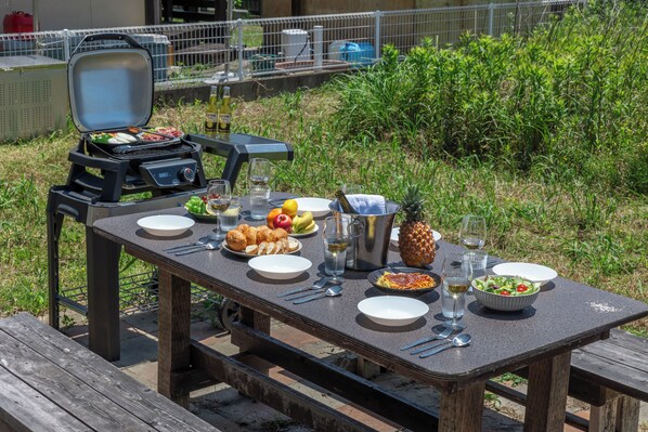 An outdoor dining table with a grill, plates, cutlery, and a variety of food and drinks. - SEASIDE HOUSE YASUTAKETEI (Shirahama)