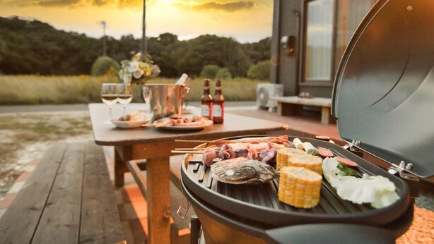 A barbecue grill with various meats and vegetables, a picnic table, and a scenic sunset view. - SEASIDE HOUSE YASUTAKETEI (Shirahama)