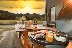 A barbecue grill with various meats and vegetables, a picnic table, and a scenic sunset view. - SEASIDE HOUSE YASUTAKETEI (Shirahama)