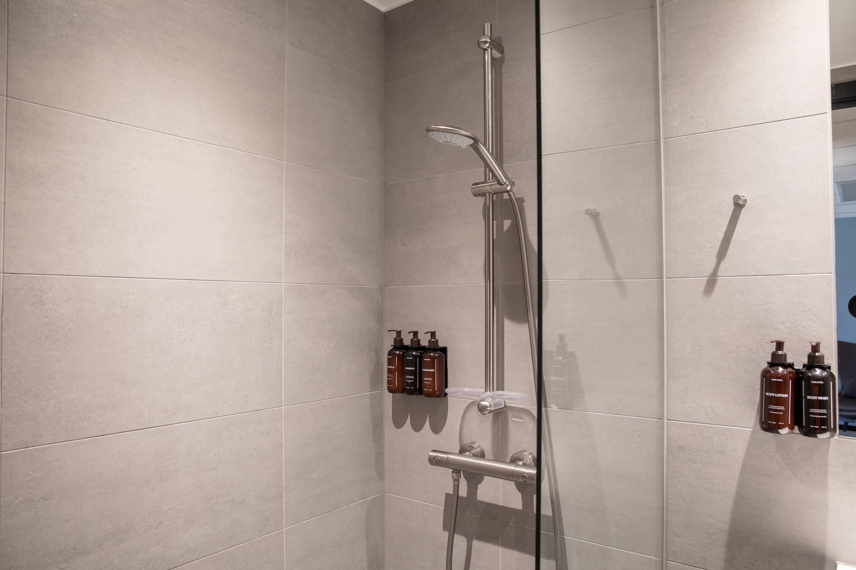 Ducha moderna con cabezal de ducha de mano y ducha de lluvia, montada en una pared con baldosas grises.