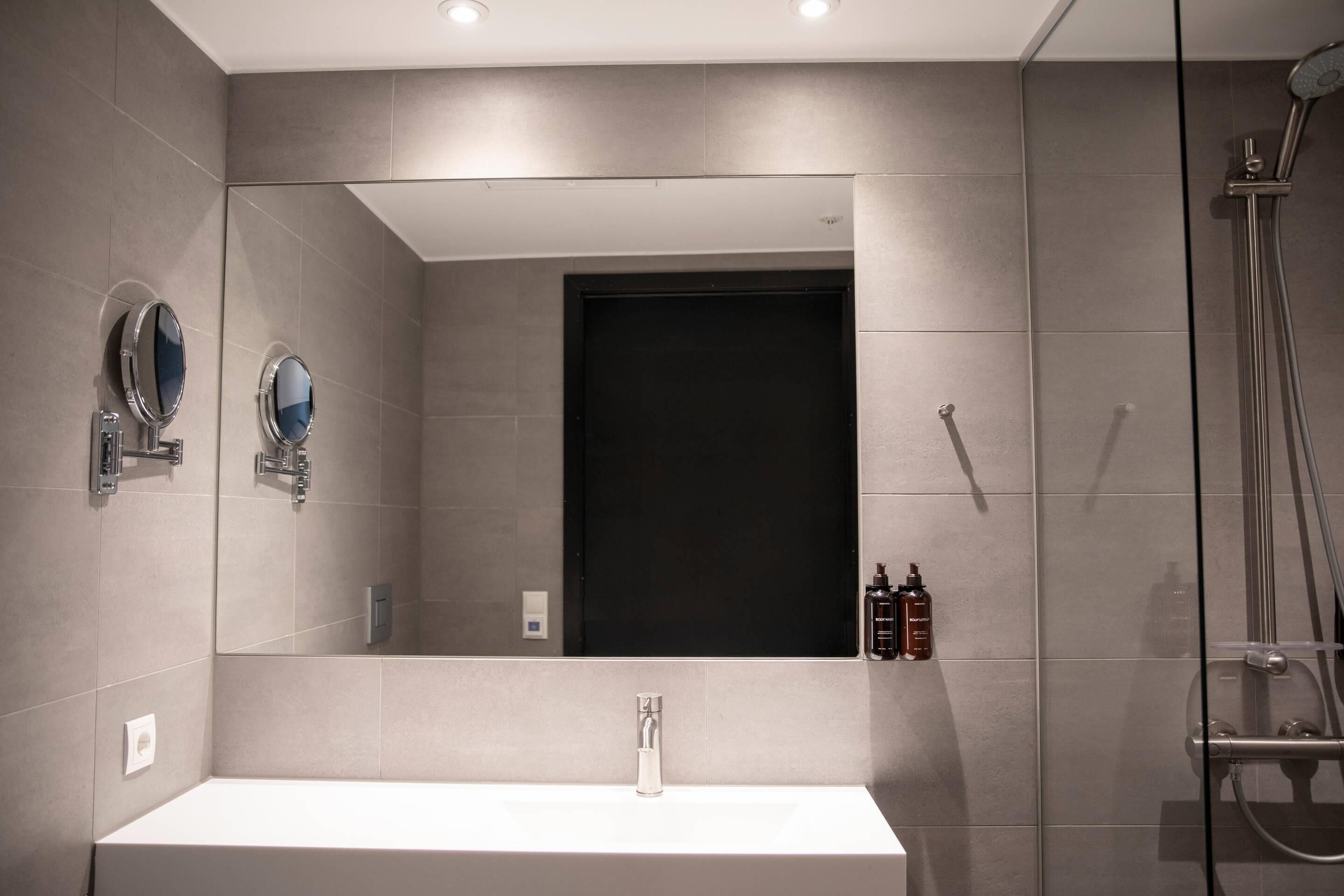 A modern bathroom with a large mirror, a sink, and a shower.