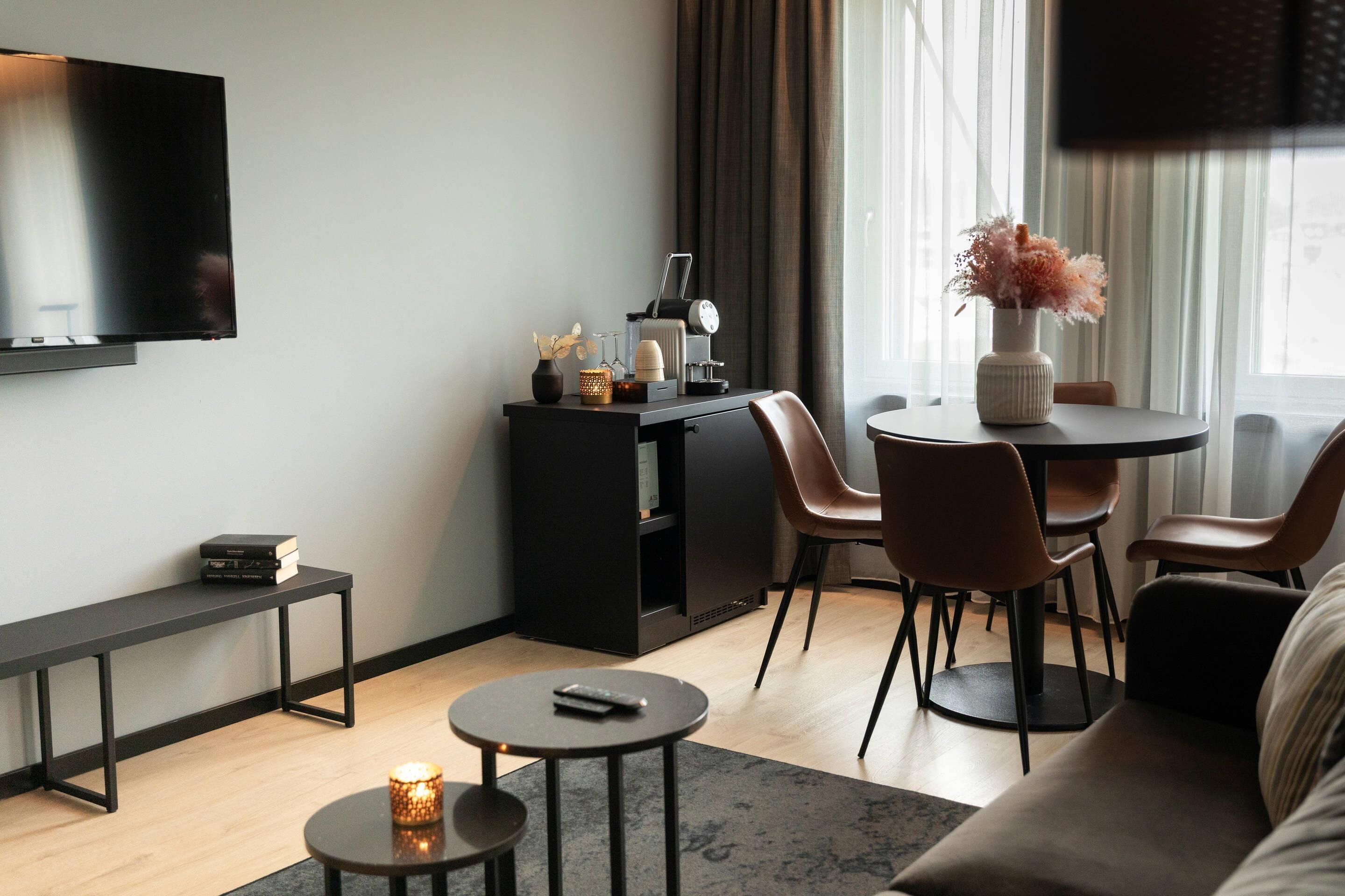 Una sala de estar moderna con un televisor de pantalla plana, una cafetera, una mesita con una vela y un sofá.