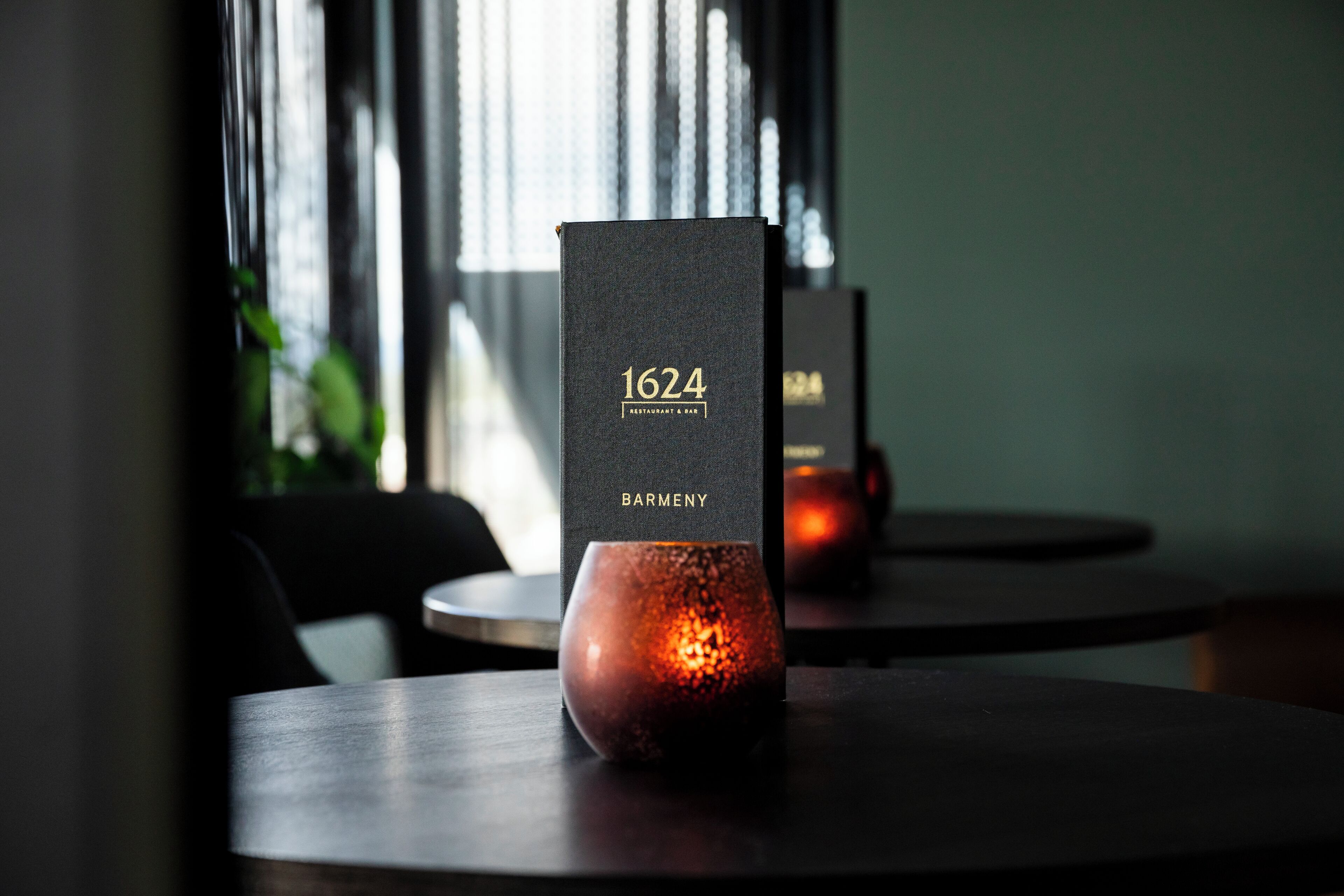 Una mesa de madera oscura con un candelabro y un atril con el menú que dice "1624 BARMENY".