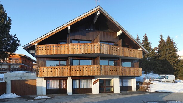 En stor chalet i trä med flera våningar, balkonger, stora fönster och en skidlift i bakgrunden.