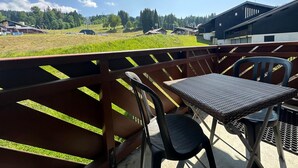 A balcony with a table and chairs, overlooking a grassy field and buildings. - Mountain apartment, sleeps 6, south balcony (Morillon 1100)