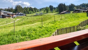 A rural landscape with a wooden fence, grassy fields, and several buildings including a large barn and a smaller structure. - Mountain apartment, sleeps 6, south balcony (Morillon 1100)