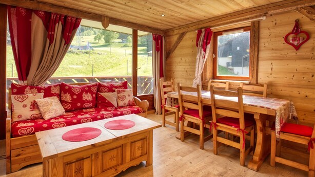 A cozy wooden cabin interior with a sofa set, wooden dining table, and chairs. - Mountain apartment, sleeps 6, south balcony (Morillon 1100)