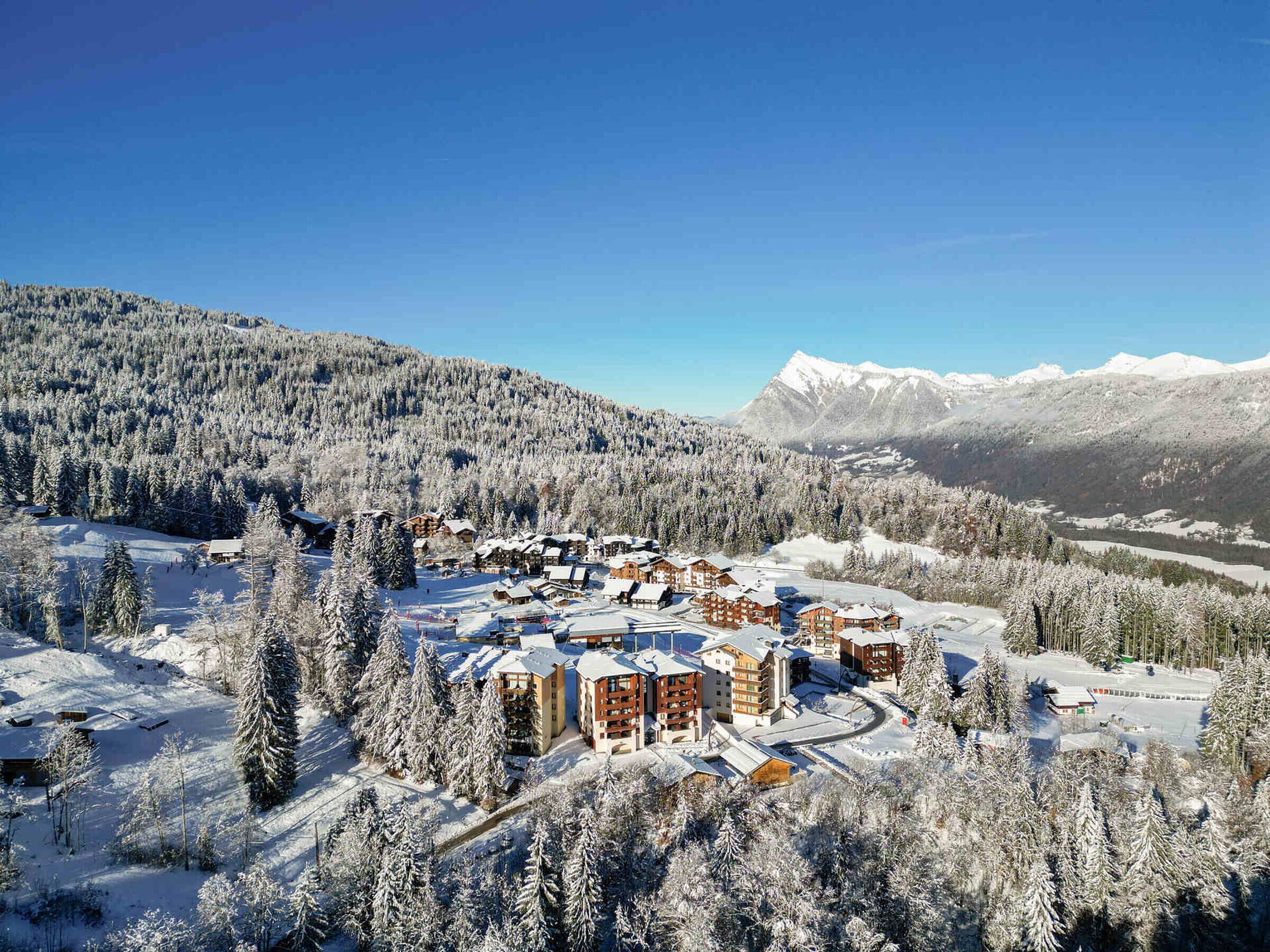 A snow-covered resort with multiple buildings, ski slopes, and a mountainous backdrop.