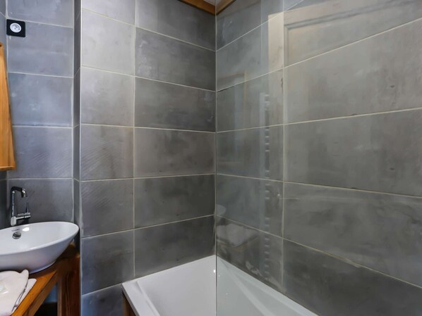 Een badkamer met grijze tegels, een wit wastafelmeubel en een bad.