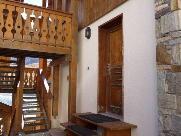 Un escalier en bois mène à une pièce dont un des murs est en pierre et qui possède une porte en bois.